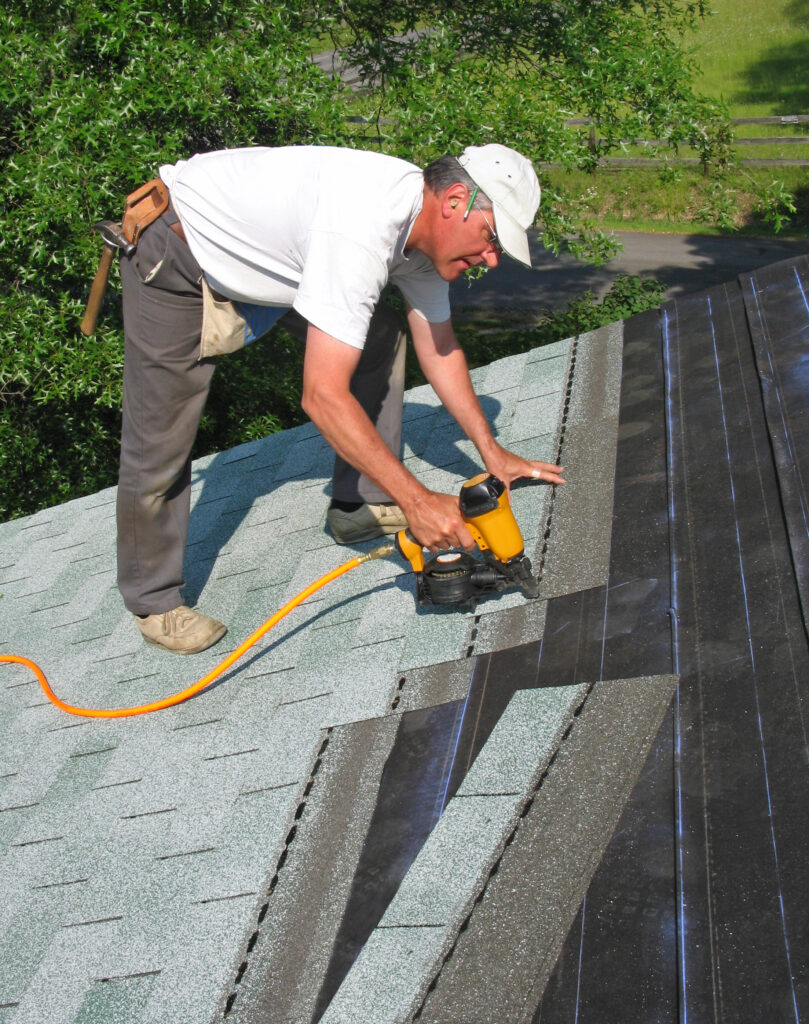 East Moline roofing carpenter using a nail gun to fix asphalt shingles to roof.